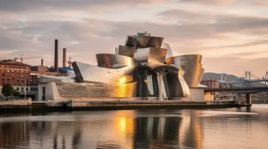 Vista panorámica del Museo Guggenheim Bilbao reflejándose en la ría del Nervión, con la ciudad industrial transformada al fondo